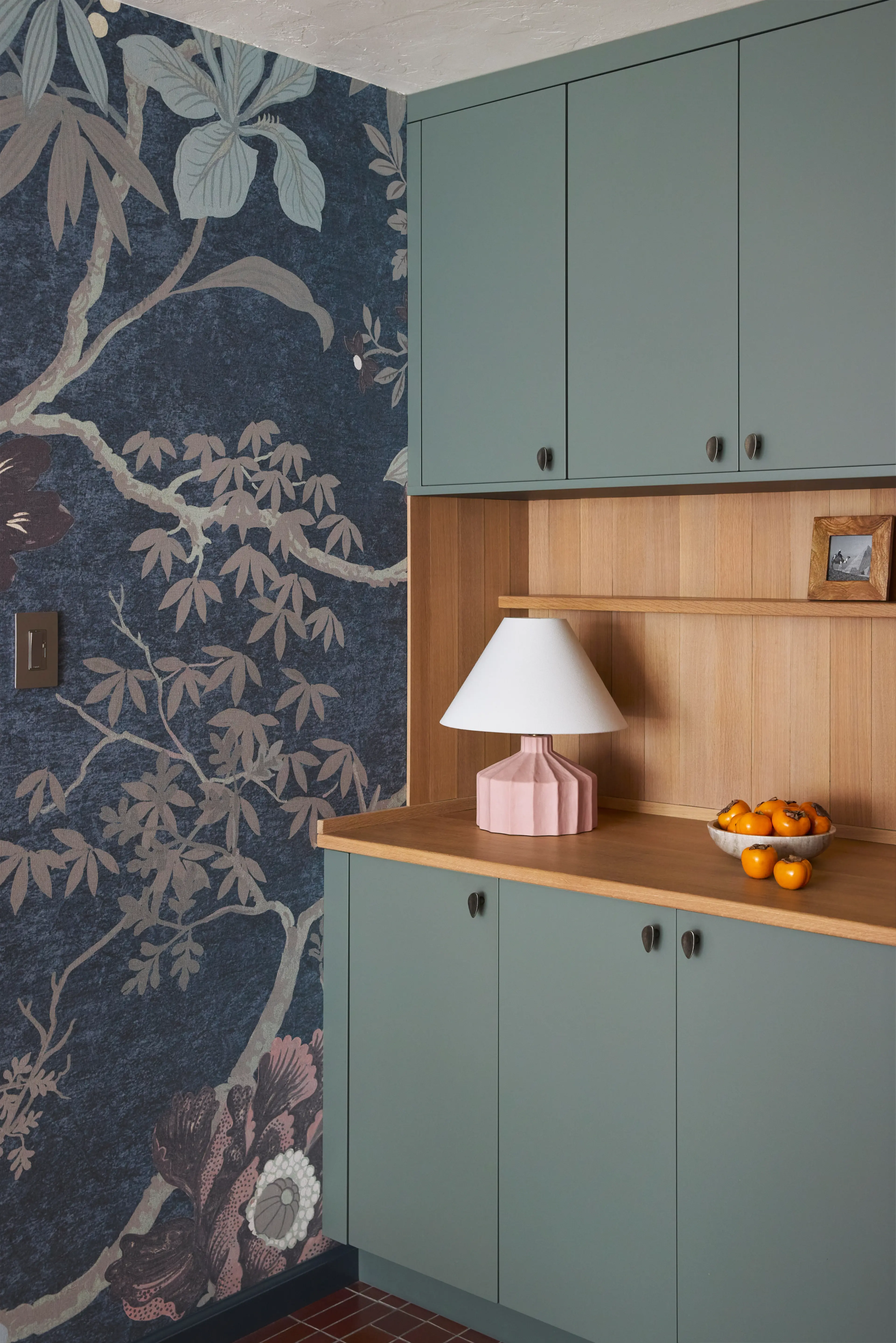 Built-in sage green cabinets and white oak surround, pink lamp, dark floral wallpaper, in a San Francisco home by Studio VAE