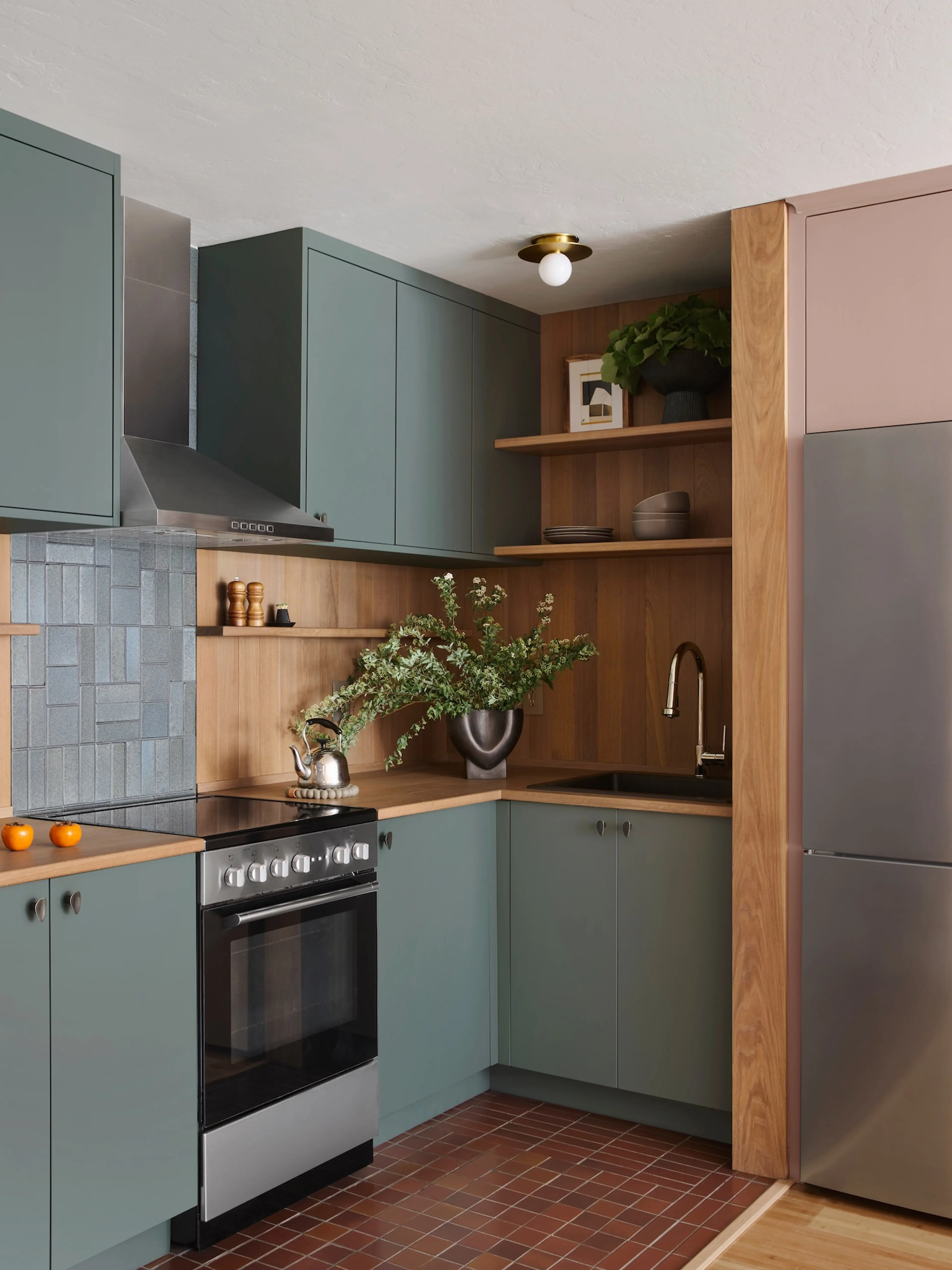 Compact L-shaped Outer Sunset kitchen with sage green cabinets, white oak surround with shelving, and terracotta floor tile